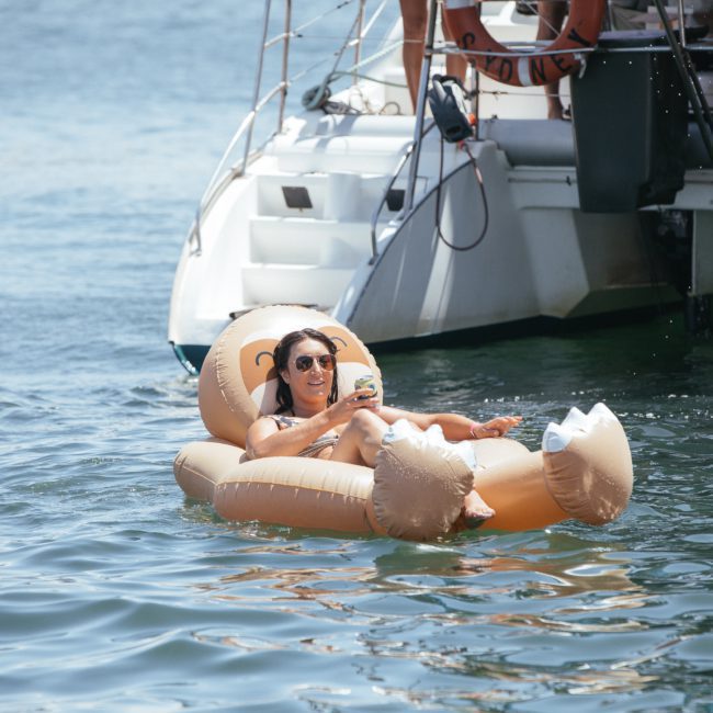A person relaxes on an inflatable float shaped like an animal while holding a drink, near a private yacht charter in Sydney Harbour.