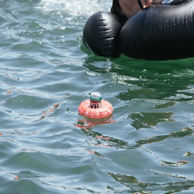 A can of beer on a small orange float in the water beside a black inflatable tube, setting the scene for an unforgettable Catamaran party Sydney.
