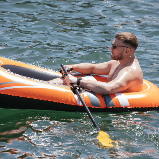 A man paddles an orange and grey inflatable boat on a body of water, enjoying the serene environment. For those seeking a more upscale experience, Luxury yacht hire Sydney offers an unforgettable adventure on the water.
