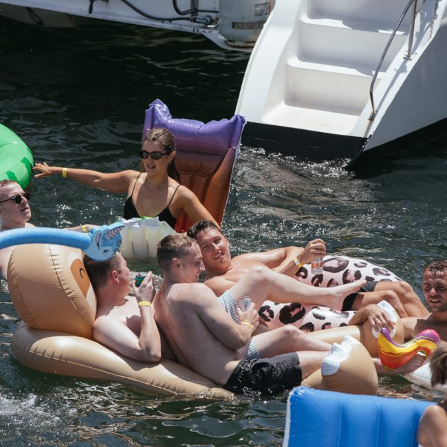 A group of people enjoying a day in the water on inflatable floats near a luxury yacht hire Sydney, with some sitting and others engaging in conversation.