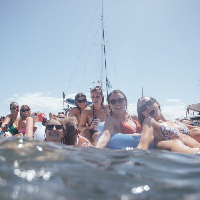 A group of people in swimwear relax on inflatable devices in the water, with boats visible in the background under a clear sky, enjoying a luxury yacht hire Sydney experience.