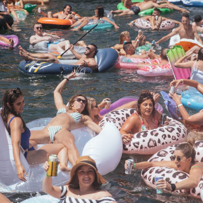 People relaxing on inflatable rafts and floats in the water, with a boat in the background bearing a "Rum Runner Cruises" sign, perfect for your next Sydney boat party hire.