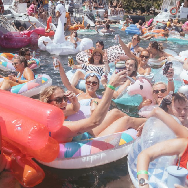 A group of people in inflatable floaties enjoy themselves in a crowded water setting with luxury yacht hire Sydney services and boats in the background.