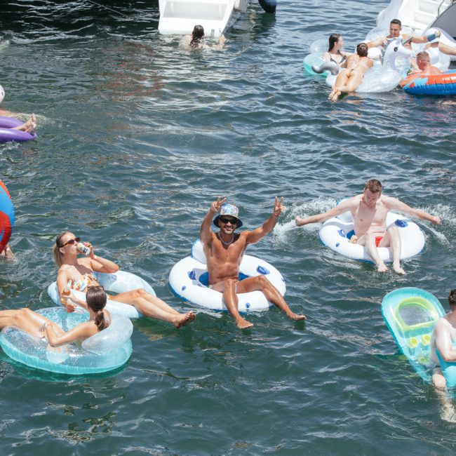 People on inflatable pool floats enjoying their time in the water, some in groups and others alone. Children and adults are present, engaging in relaxed and playful activities near a private yacht charter Sydney Harbour.