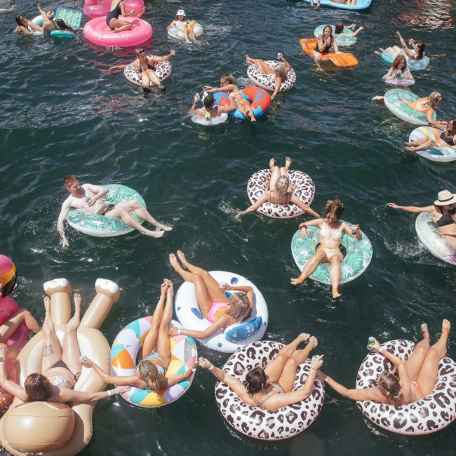 Aerial view of people relaxing on colorful inflatable rings and loungers in a body of water on a sunny day, near a private yacht charter Sydney Harbour.