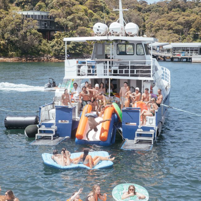 People enjoying a sunny day on a private yacht charter in Sydney Harbour, floating on inflatable loungers, swimming in the water, and having the best time of their lives.