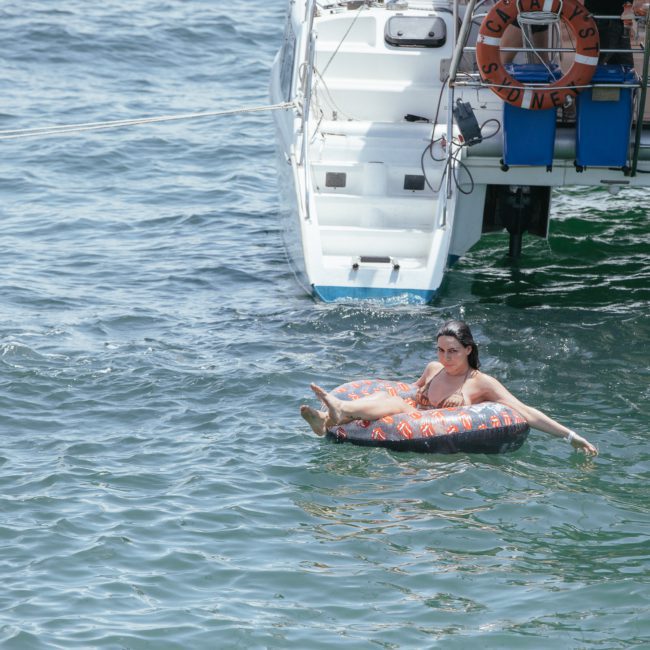 A person relaxes on an inflatable tube in the water near boats during a lively catamaran party in Sydney.