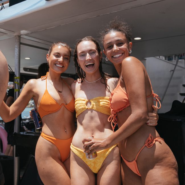 Three people in swimsuits smiling and posing together on a luxury yacht hire Sydney.