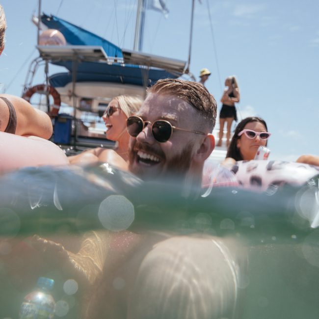 People enjoying a sunny day in the water near a luxury yacht hire in Sydney Harbour. Some are using flotation devices.