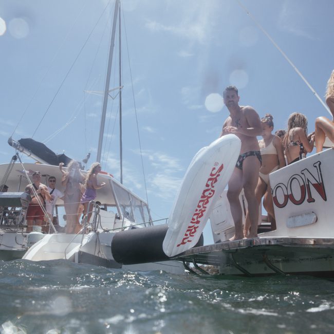 People in swimsuits on and around a boat, with one person holding an inflatable float. The group appears to be enjoying a day on the water during a perfect Sydney boat party hire.