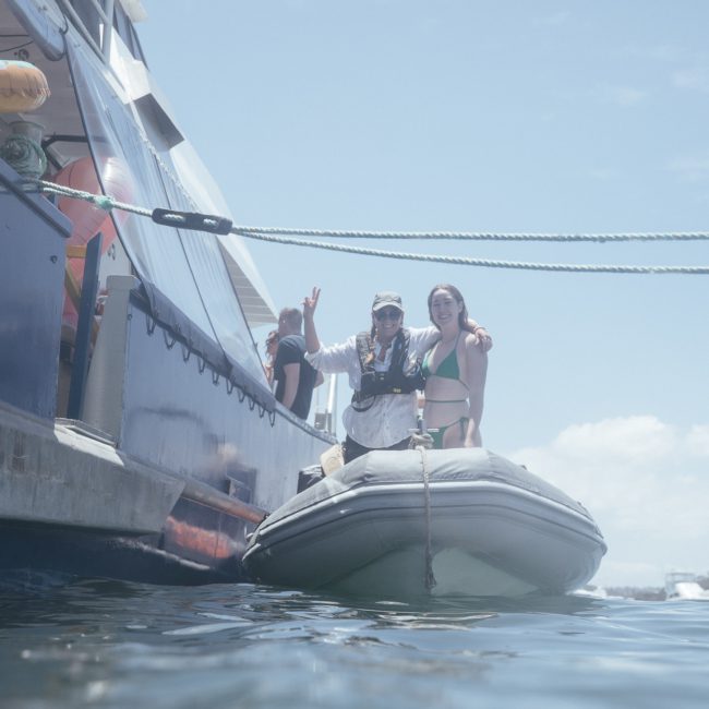 Two people stand on a small inflatable boat docked beside a luxurious yacht in Sydney's waters on a sunny day, showcasing the perfect backdrop for corporate boat events.