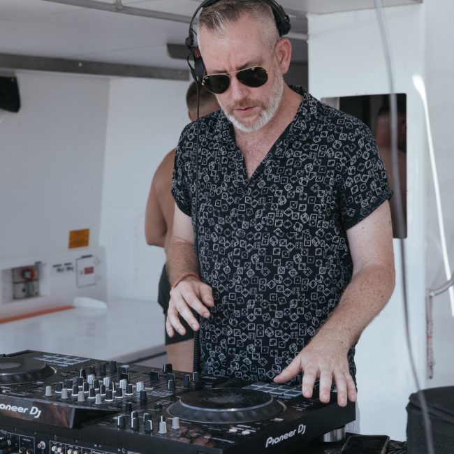A DJ wearing sunglasses and headphones is mixing music on a Pioneer DJ controller during a luxury yacht hire Sydney event.