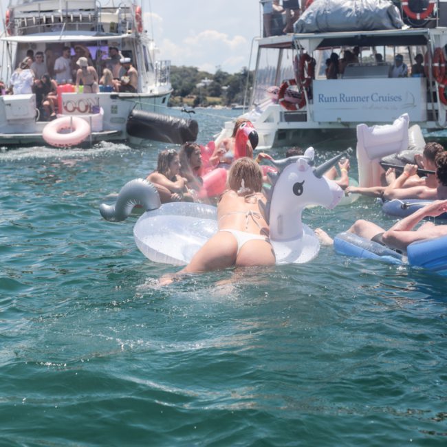 People enjoying a summer day on a lake, floating on inflatable rafts and swim rings near a luxurious yacht from Sydney boat party hire.