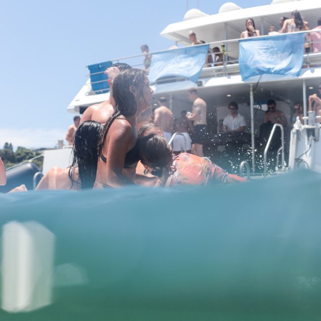 People swimming near a boat in the water, with others on the boat in the background. The "Yacht Social" logo is visible in the lower right corner. Experience a memorable day with our luxury yacht hire Sydney services.
