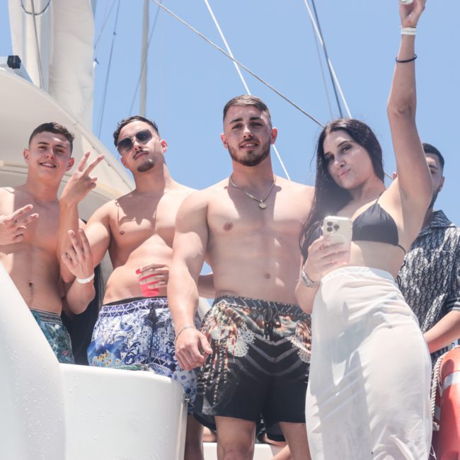 A group of young adults on a boat, some shirtless, posing for a photo; one person takes a selfie during an exciting Sydney boat party hire.