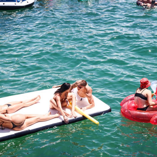 People relaxing on inflatable floats and rafts in a body of water on a sunny day, enjoying a beautiful backdrop that makes it feel like a luxury yacht hire in Sydney.