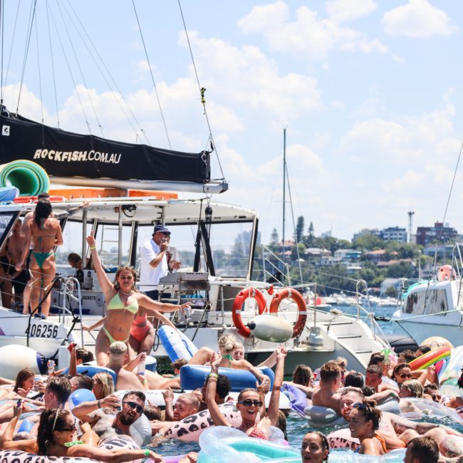 A lively pool party on boats in Sydney, with people swimming and floating on inflatables under a clear sky, featuring DJ boat hire Sydney for an unforgettable experience.