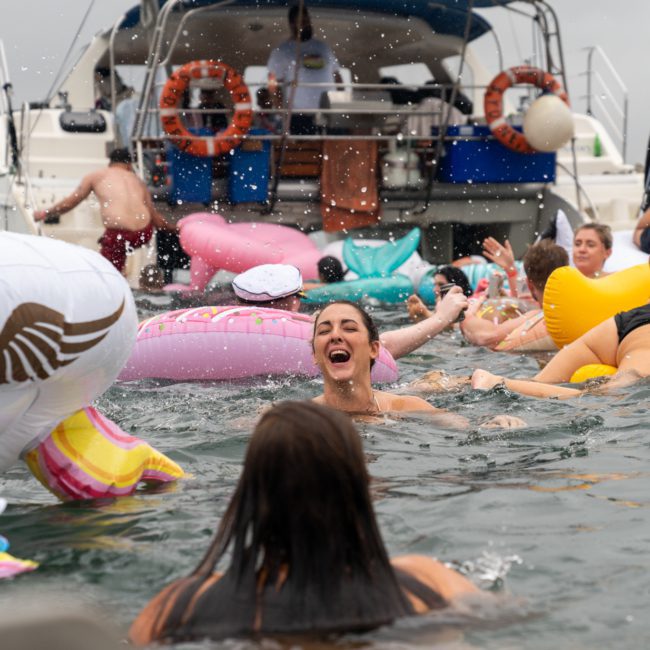 A group of people swim and float on inflatable toys in the water near a private yacht charter on Sydney Harbour.