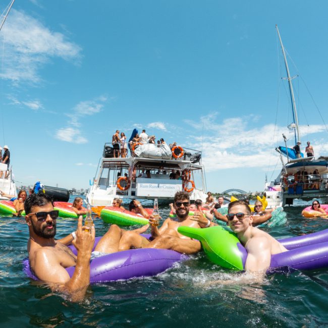 A lively group of people relaxing on inflatable rafts in the water, surrounded by several boats and enjoying the sunny day, epitomizes a perfect Sydney boat party hire. The scene is enhanced by a luxurious private yacht charter in Sydney Harbour.