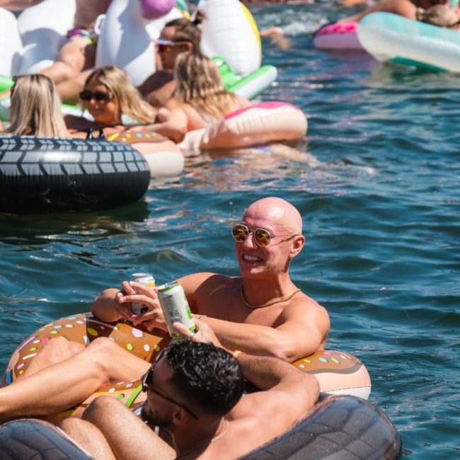 People floating on inflatable pool floats in a body of water, with one person holding a drink can and smiling during a luxurious private yacht charter Sydney Harbour.