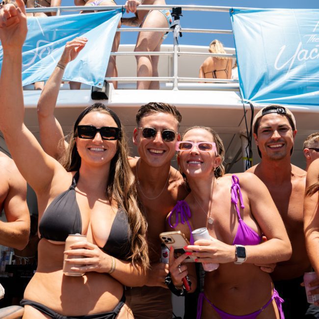 A group of people in swimwear, smiling and posing for a photo aboard a yacht with "The Yacht Social Club" banners in the background, perfect for Corporate boat events Sydney.