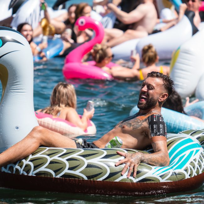 Multiple people are seen floating on inflatable pool toys in a body of water, some laughing and enjoying themselves. The pool toys are shaped like various birds and animals, adding to the festive atmosphere—perfect for a Sydney boat party hire or corporate boat events Sydney.