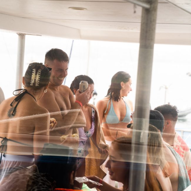 A group of people in swimwear socialize on a luxury yacht hire Sydney, chatting and taking pictures.