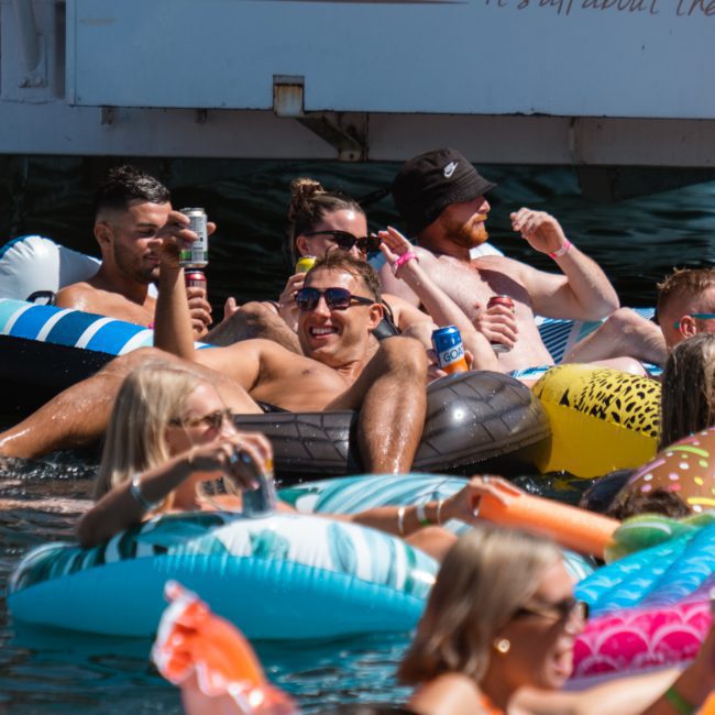A group of people relax on inflatable tubes in the water, holding drinks and enjoying sunny weather near a luxury yacht hire Sydney.