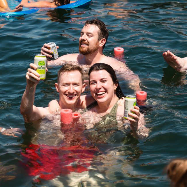 A group of people enjoying a DJ boat hire on Sydney Harbour, holding cans and foam.