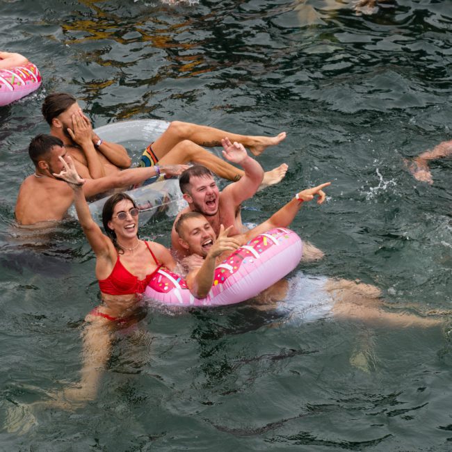 A group of people in the water enjoy themselves with inflatable tubes, smiling and pointing. Some wear swimsuits and others just swim, creating a lively and joyful atmosphere reminiscent of a Sydney boat party hire.