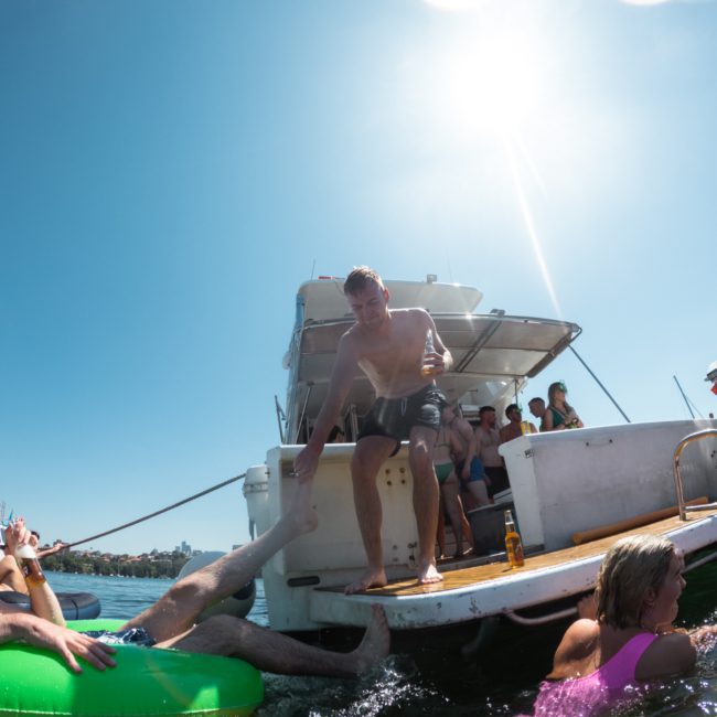 People enjoying a sunny day on a private yacht charter in Sydney Harbour, with some swimming and lounging on floatation devices in the water.