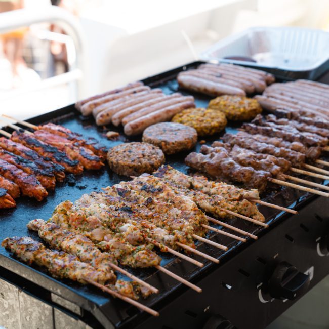 Assorted meats including skewers, sausages, and patties cook on a large outdoor grill during a private yacht charter in Sydney Harbour.