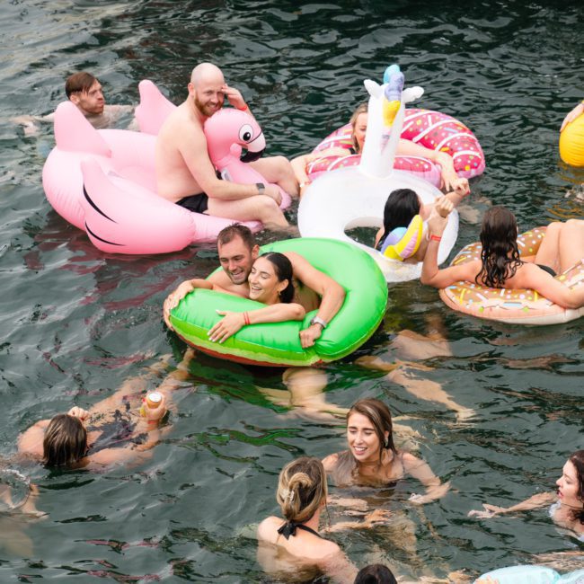 People are swimming and floating on inflatable toys in a body of water, with some engaged in conversation and enjoying the scene, similar to the vibrant atmosphere you'd find at a Sydney boat party hire.