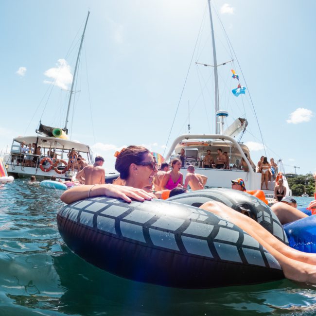 People relaxing on inflatable floats and enjoying themselves in the water near anchored boats on a sunny day, creating a perfect scene for a luxury yacht hire Sydney.