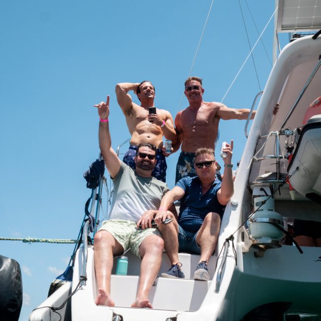 Four men are posing on the back of a boat in swimwear, with some flexing their muscles. It is a sunny day with clear blue skies, perfect for a luxury yacht hire Sydney experience.
