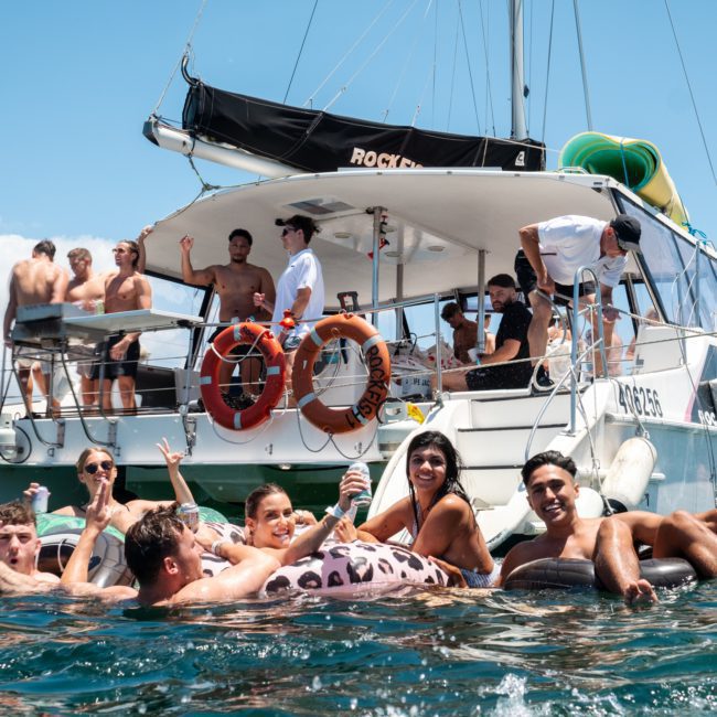 People relax and socialize on a luxury yacht hire in Sydney, both on the vessel and in the water, enjoying a sunny day.