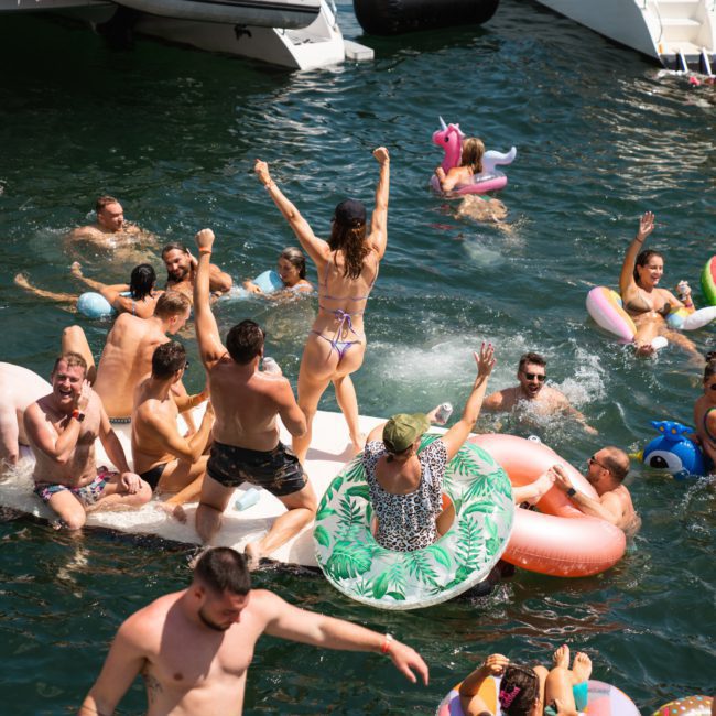 People enjoying a lively time in the water with various floaties and inflatable toys near boats, perfect for those on a private yacht charter Sydney Harbour.