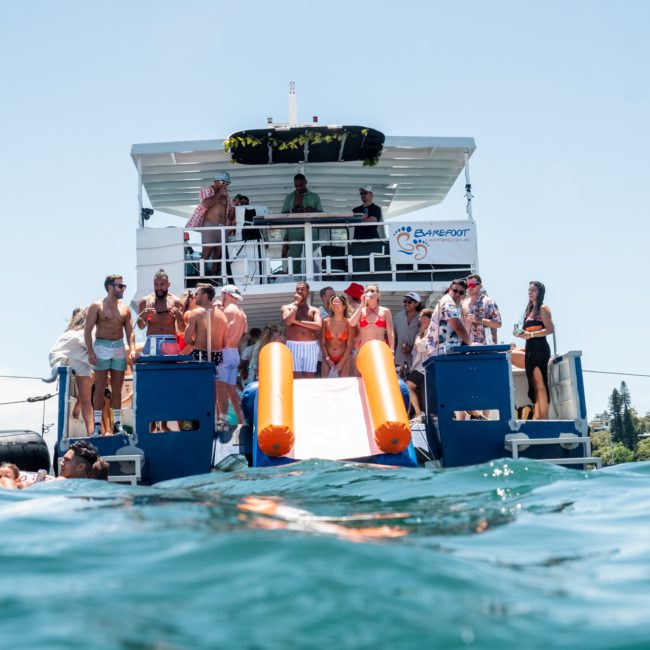 People enjoying water activities and socializing on a Catamaran party Sydney, with dual slides into the water, surrounded by a clear blue sea.