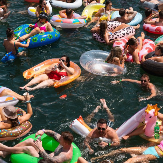 A lively gathering of people on various inflatable pool floats, including unicorns, flamingos, and donuts, enjoying themselves in a body of water. Ideal for a catamaran party in Sydney or even a private yacht charter on Sydney Harbour for that unforgettable experience.