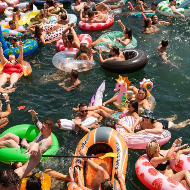 People enjoying a sunny day in the water with colorful inflatable floats, including unicorns, ducks, and donuts, alongside a luxury yacht hire Sydney.