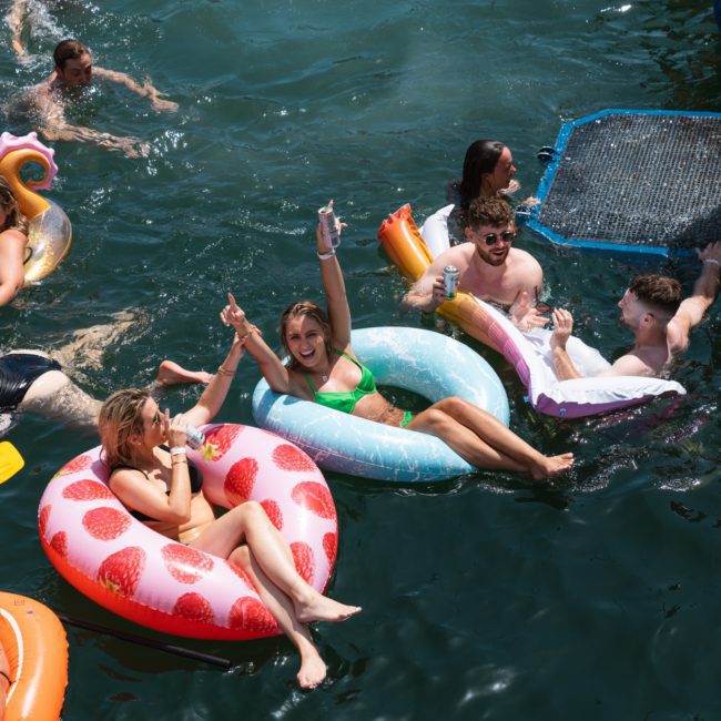 People are lounging on inflatable floats in a body of water, some with drinks in hand, enjoying a sunny day during a private yacht charter on Sydney Harbour.