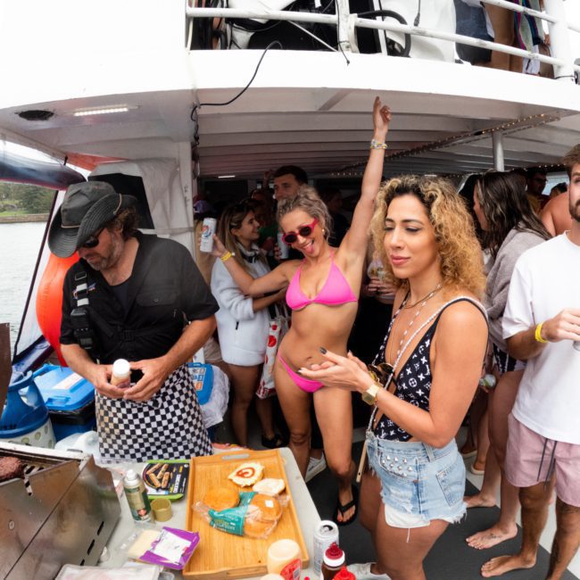 Group of people enjoying a boat party in Sydney, some dancing and others socializing near a grill with food and drinks on a luxury yacht hire.
