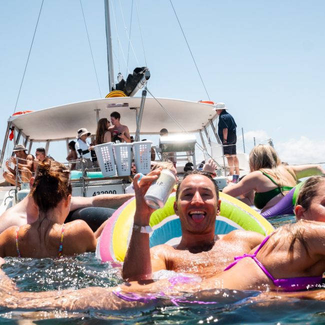 People enjoying themselves on a luxury yacht in the water with inflatable tubes and swimsuits, under a clear sky.