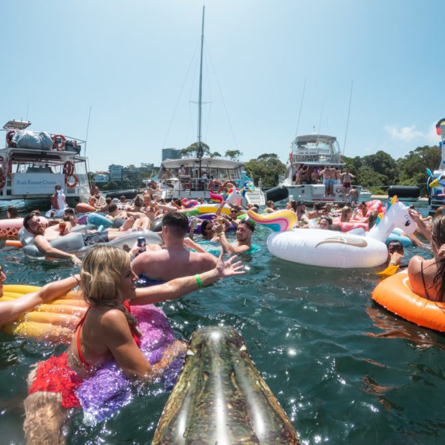 A lively group of people enjoying a sunny day on the water, floating on various inflatables and surrounded by several boats––a true Sydney boat party hire experience.