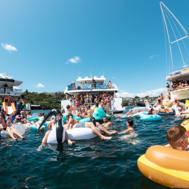 People enjoying a sunny day on the water, floating on inflatables near boats during an exciting Catamaran party Sydney.