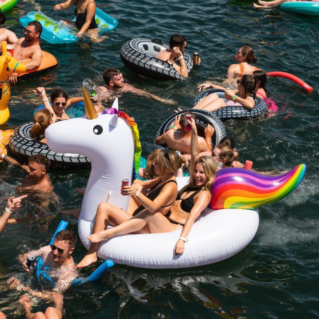 People on various inflatable rafts, including a unicorn float, socialize and relax in a crowded water area, while others enjoy the luxury yacht hire Sydney offers.