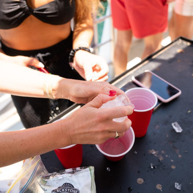 Close-up of people preparing drinks with red cups and ice at an outdoor gathering. A bag of five grains is visible on the table along with a phone, giving the scene a lively, festive atmosphere reminiscent of a Sydney boat party hire.