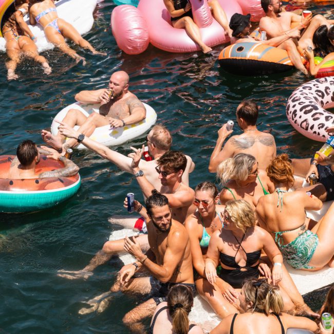 A group of people enjoying a sunny day on a lake, lounging on an assortment of colorful inflatable floats and socializing in the water, reminiscent of the vibrant ambiance found during corporate boat events in Sydney.