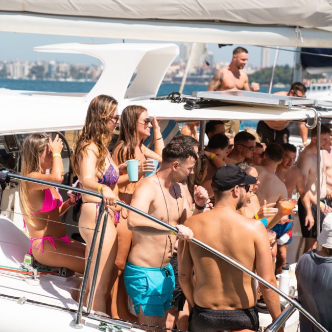 A group of people in swimwear gathered on a luxury yacht in Sydney Harbour under sunny weather, some holding drinks.