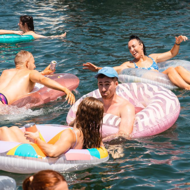 A group of people relax on inflatable pool floats in a body of water on a sunny day, chatting and enjoying each other's company during a private yacht charter on Sydney Harbour.